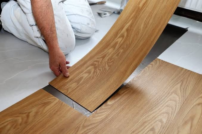 Handwerker verlegt eine Bodenplanke in Holzoptik auf einem hellen Untergrund (Symbolfoto)